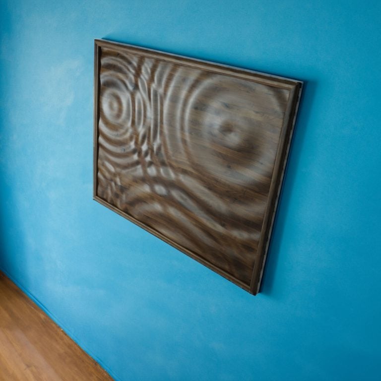 Wood wall art with a water drop pattern. The wood is solid walnut and this is a large fourty eight inch by sixty inch piece. This piece is hanging on a deep blue wall of a restaurant By Timeworn.